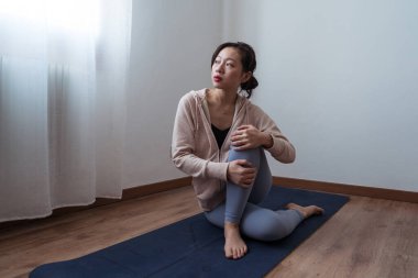 Atletik giyinen genç bir kadın dinlenme odasında yoga minderinde otururken düşünmek için ara verir.