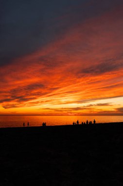 Turist siluetlerinin kıyıdan sonsuz okyanusa hayran olduğu manzara bulutlu gökyüzünün altından alacakaranlıkta parlayan güneşle
