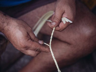 Palmito sepetleri dokumak gibi karmaşık bir beceri gerektiren bu yakın plan, geleneksel zanaatkarlığı sergilemek için palmito şeritlerini dikkatle manipüle eden bir zanaatkarın ellerini vurguluyor.