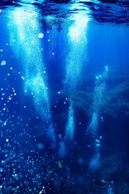 Menorca 'da tatilin tadını çıkarırken baloncuklar ve kayalar arasında derin mavi okyanusa dalan tanınmayan dalgıçların uzak görüntüsü