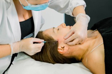 Profesyonel kozmetik uzmanı, estetik kliniğindeki bir hastaya hiyalüronik asit ve tensör iplikçikleriyle yüz tedavisi uyguluyor.