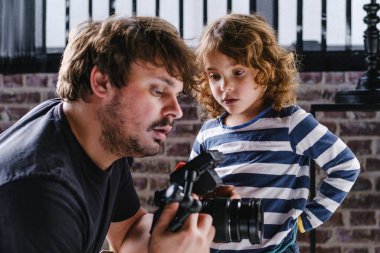 Genç yetişkin bir erkek film yapımcısı, meraklı bir çocukla kameradaki görüntüleri inceliyor.