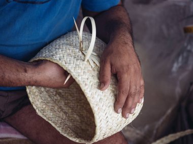 Palmito iplikçiklerinden narin bir sepet ören bir zanaatkarın detaylı yakın çekimi, karmaşık el işi ve geleneksel zanaat becerileri.