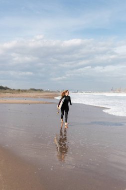Eğitim sırasında ıslak sahilde dalgalı deniz kenarında siyah dalgıç kıyafetiyle koşan sportif kadın sörfçülerin tüm vücudu.