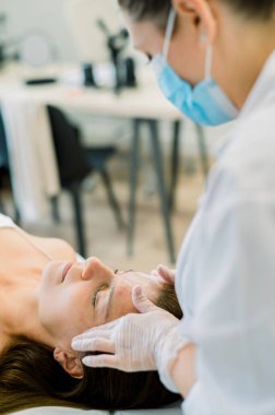 Pratisyen hyaluronik asit, botoks veya tensör ipliklerini estetik klinikte uygulamadan önce hastanın alnını nazikçe muayene eder.