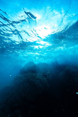 Menorca koylarında parlak güneş ışığı olan şeffaf mavi okyanusun dibindeki devasa kaya oluşumlarının sualtı görüntüsü.