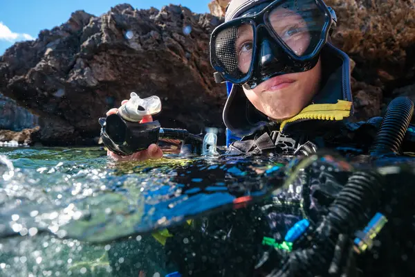 Yaz tatilinde okyanusta kaya oluşumlarına karşı yüzerken dalgıç kıyafetli ve maskeli anonim genç erkek portresi.