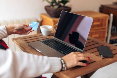 Masada dizüstü bilgisayarla oturan ve modern evde yeni bir proje üzerinde çalışırken kredi kartı bilgilerini yazan isimsiz genç serbest kadın.