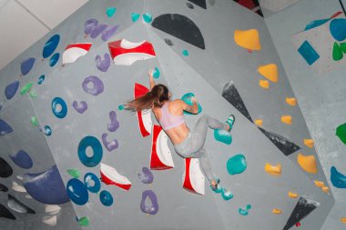 Atletik bir kadın renkli bir kaya duvarına tırmanıyor, dayanıklılık ve konsantrasyon gösteriyor..