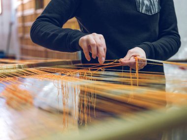 Close-up of hands manually weaving yarn on a loom in a traditional textile factory with an anonymous worker clipart