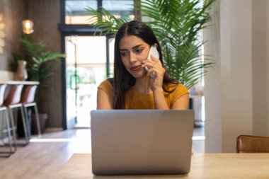 Kafenin ahşap masasında oturan ve netbook 'ta yazı yazarken gözlerini kaçıran ciddi bir serbest çalışan kadın.