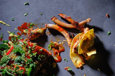 Üst görüntüde taze otlarla süslenmiş leziz pirzola tacoları, koyu bir arka planda biraz sos ve kaburga kemikleri var..