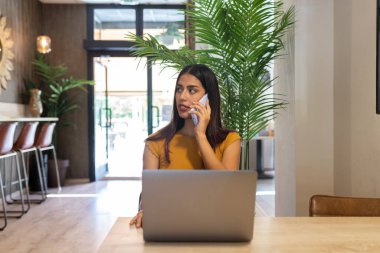 Kafenin ahşap masasında oturan ve netbook 'ta yazı yazarken gözlerini kaçıran ciddi bir serbest çalışan kadın.