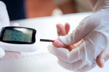 Bir sağlık uzmanı, şeker seviyesini kontrol etmek için hasta parmağına kan şekeri testi yapar ve hipoglisemi belirtilerini ölçer.