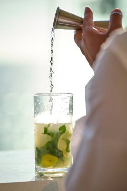 Buzlu, nane yapraklı ve ferahlatıcı yaz içeceklerini tasvir etmek için ideal taze limon dilimleriyle dolu bir viski bardağına rom döker.