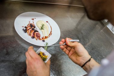 Şefin ellerinin üst görüntüsü titizlikle son bir dokunuşla güzel bir tabak kızarmış ördek göğsüne patates püresi ve böğürtlen sosu ekler..