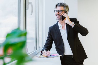 Neşeli bir yönetici bir iş görüşmesine katılır, penceresinin kenarına notlar alır.