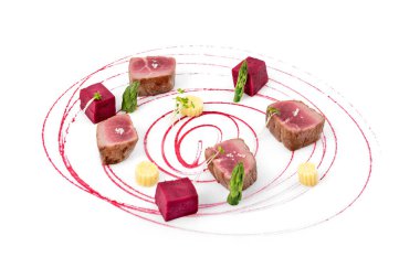 Kuşkonmaz ve dekoratif pancar sosuyla bezenmiş kırmızı ton balığı parçalarının sanatsal sunumu, beyaz bir arka planda otlar ve pancar küpleriyle süslenmiş.