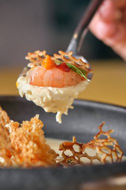 Lezzetli bir garnitürle süslenmiş lezzetli bir karidesin yer aldığı, kremalı sos ve çıtır çıtır tempura ile eşleştirilmiş bir gurme yemek deneyimi, yemeğin dokusunu ve canlı renklerini vurgulamak için yakın plan çekimde yakalanır.