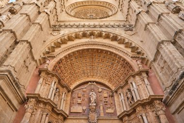 Mallorca Katedrali 'nin Majestic cephesinden, ayrıntılı taş heykellerle çevrili belirgin bir heykel ile karışık Gotik mimarinin yer aldığı La Almudaina Kraliyet Sarayı' nın arka planına karşı..