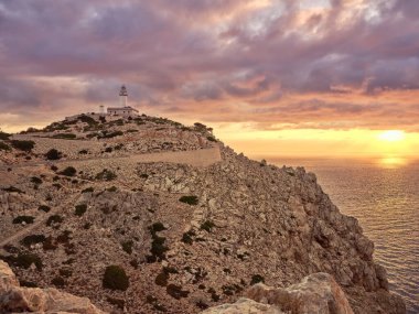 Günbatımı, Mallorca 'nın en kuzeyindeki Cape Formentor deniz fenerini çevreleyerek engebeli kıyı şeridini ve sakin gökyüzünü aydınlatır..