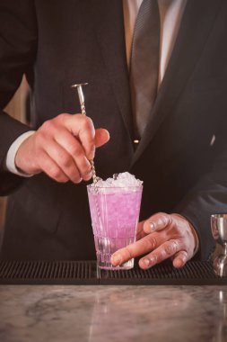 Siyah takım elbiseli meçhul erkek barmen barda kaşıkla kokteyl karıştırıyor.