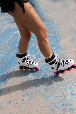 Kaykay parkında beton kaldırımda duran pembe tekerli beyaz patenli anonim kadın bacakları.