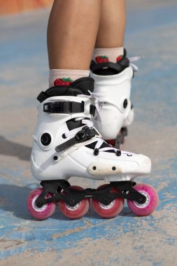 Kaykay parkında beton kaldırımda duran pembe tekerli beyaz patenli anonim kadın bacakları.