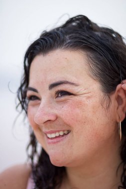 Gülümseyen kavisli kadın ıslak dalgalı saçlarını düzeltiyor ve bulanık arka plana bakıyor.