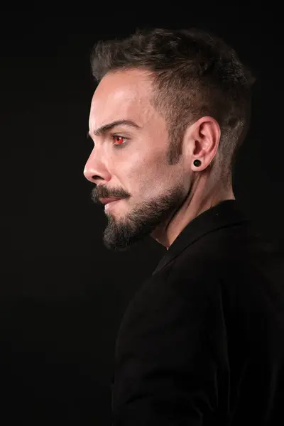 stock image A man with a beard and styled hair posing in profile against a dark background with red contact lenses