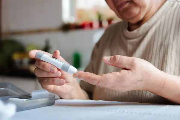 stock image A senior woman is using a glucometer to check her blood sugar levels at home, indicating a focus on managing hypoglycemia