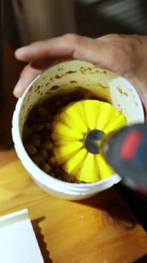 El yapımı elektrikli matkapla tanınmaz hale getirilmiş bir adam mikro yeşillik yetiştirmek için koni şeklinde öğütücüye nohut tohumları yerleştiriyor. Matkabın hareketi tohumları ve öğütücü bileşenleri bulanıklaştırarak dinamik iş akışını arttırır.