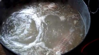 Geleneksel domuz kesim sürecinin bir parçası olarak büyük bir tencerede kaynayan et fokurdayan su ve retiküle edilmiş kaplar, domuz ürünlerinin zanaatkar üretimini ön plana çıkarıyor.