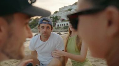 Genç bir çift, arka planda kumlu bir plaj ve beyaz yamaç evleri olan selfie çekerken sıcak bir şekilde gülümsüyor ve mükemmel bir yaz anını yakalıyor.