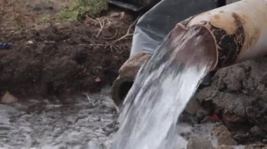 Çamurlu bir araziye dökülen paslı bir borudan akan su, tarım alanındaki sulama uygulamalarını ve toprak yönetimini betimliyordu.