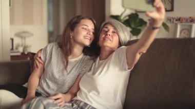 Anne ve kızı kanepede mutlu bir anı paylaşıyor, birlikte selfie çekerken gülümsüyorlar, ifadeleri sevgiyi ve bağlantıyı gösteriyor, özel bağlarını ve birlikte olmanın sevincini kutluyorlar.