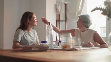 Bir anne, kızının saçına nazikçe dokunur. Mutfak masasında otururken keyifli bir anı paylaşırlar. Sohbete dalarlar.