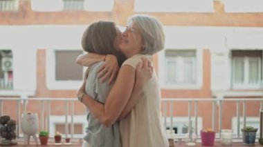 Bir anne ve kızın sıcak, sevgi dolu bir kucaklaşmayı paylaştığı huzurlu bir an, yüzleri mutluluk ve sevgiyi ifade ediyor.