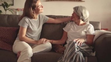 Bir anne ve kızı evdeki bir kanepede otururken sıcak bir kucaklaşmayı paylaşırlar. Sahne, güçlü bağlarını ve sevgilerini yansıtan bir sevgi, bağlantı ve yakınlık anını yakalar.