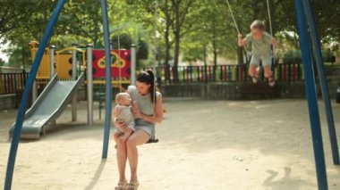 Beyaz bir anne bebeğiyle salıncaktan hoşlanırken, büyük oğlu oyun sahasında tek başına sallanıyor..