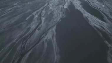 Çarpıcı bir hava fotoğrafı, koyu ve gümüşi çökeltilerin gradyanlarıyla işaretlenmiş dağlık bir bölgeden akan örülmüş nehirlerin kompleks ve iç içe geçmiş desenlerini gösteriyor.