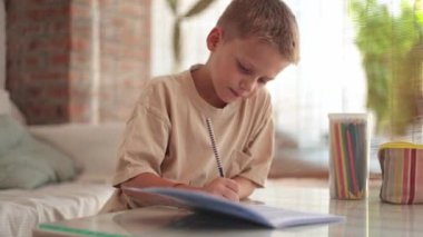 Kafkasyalı bir çocuk, gerçek zamanlı öğrenmeye dalmış, ödevini iyi aydınlatılmış bir odada, elinde bir kalem ve yanında renkli bir kalem kılıfıyla özenle yapıyor..