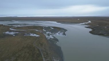 Uçsuz bucaksız dağlık bir arazide süzülen geniş nehir ağını gösteren hava manzarası bulutlarla kaplı bir gökyüzünün altında sakin ve el değmemiş bir ortamı çağrıştırıyor.