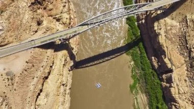 Beyaz Kanyon 'daki çamurlu Colorado Nehri' ni kaplayan bir köprünün kuş bakışı görüntüsü Glen Kanyonu Ulusal Rekreasyon Bölgesi 'nde doğal engebeli arazileri ve sularda yüzen küçük bir tekneyi yakalıyor.