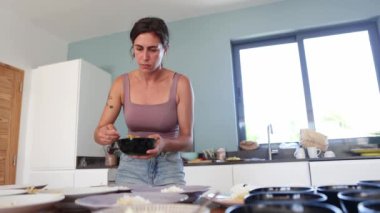 Odaklanmış bir kadın, güneşli, modern bir mutfakta sağlıklı bir yemek hazırlıyor, yiyecekleri dikkatlice konteynırlara bölüyor.