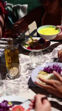 Bir insan sağlıklı beslenmeye odaklanmış bir atölyede çeşitli sağlıklı yiyeceklerin üzerine sarı sos döker. Masada parlak doğal ışık altında kırmızı lahana gibi çeşitli taze malzemeler sergilenir.