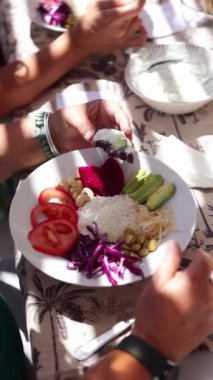 Katılımcılar sağlıklı bir beslenme atölyesinde sebze, pirinç ve kaju dolu bir tabağı doğal güneş ışığı altında sergileyerek vejetaryen yemeğinin tadını çıkarıyorlar.