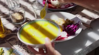 Sağlıklı beslenme atölyesinin yakın çekim görüntüsü, taze, çeşitli malzemelerin üzerine besleyici sarı bir sos döken ellerin altını çizmek, ve temel yemek yağları.