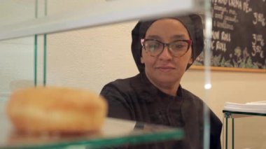 Uzman bir fırıncı, fırın vitrininde düzgünce yerleştirilmiş bir kutuda el yapımı vejetaryen çörekleri servis ediyor.