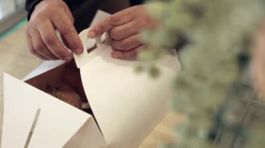 Bu videoda, bir satıcı, vejetaryen donutları titizlikle paketleyip paket servisi için ideal beyaz bir karton kutuya koyar.